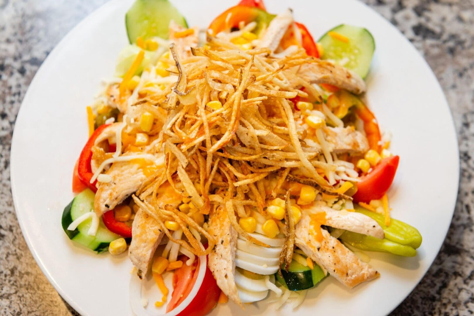 A salad with chicken, corn and tomatoes on top.