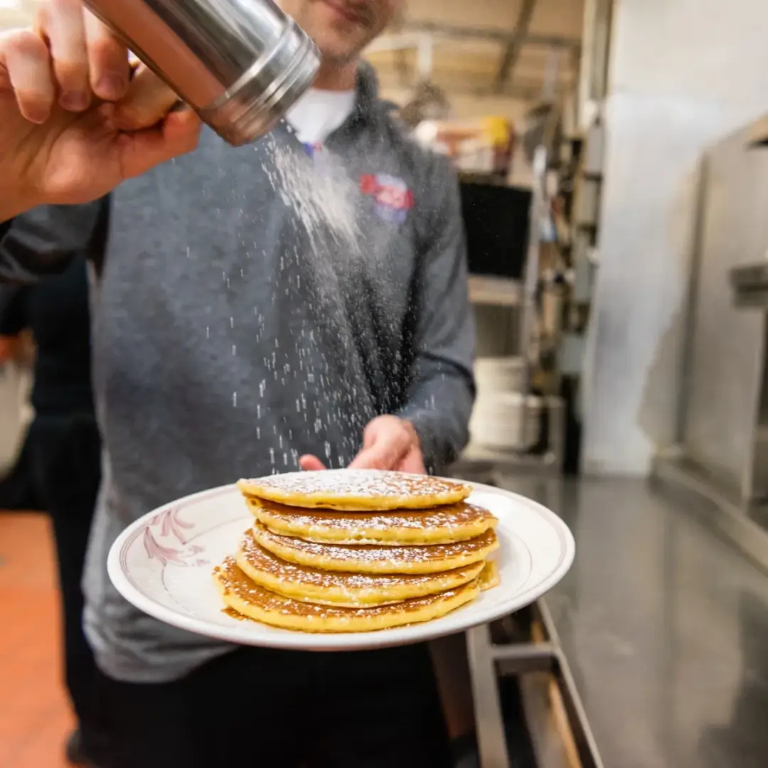 A person pouring powdered sugar on pancakes.