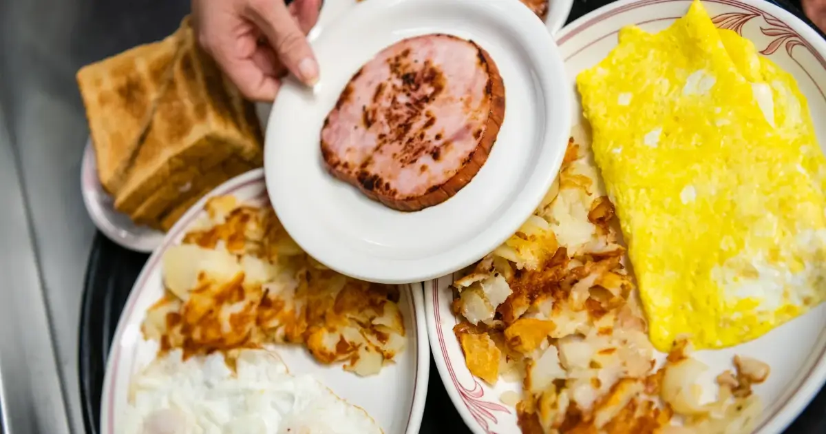 A person is holding a ham on top of a plate.